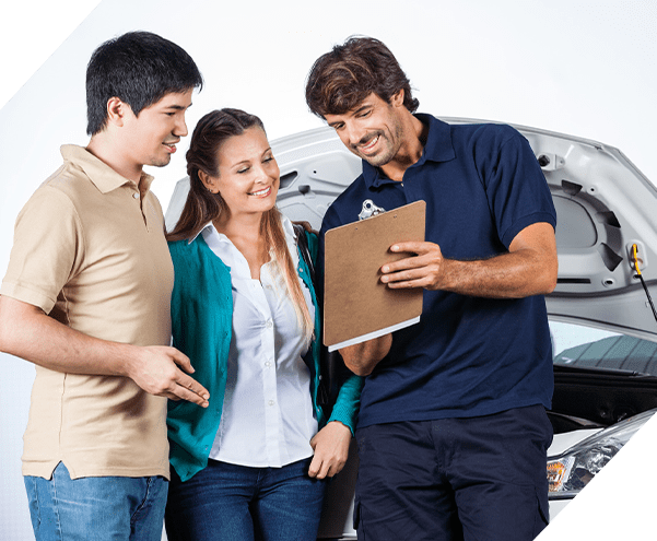 Happy male mechanic explaining documents to couple in auto repair shop